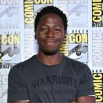 David Jonsson, the new Black Panther, stands in front of a Comic-Con International hoarding featuring a repeating pattern of