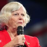 Ann Widdecombe wears a red jacket and holds a microphone while speaking at the Reform Party 2024 Conference