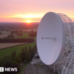 An aerial view at sunrise of the Lovell telescope at Jodrell Bank. Its huge white dish, taller than a house, is tilted