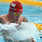 Adam Ramsay-Peaty, wearing a red Speedo swimming cap and goggles, swims in the pool during the 50m men's breaststroke