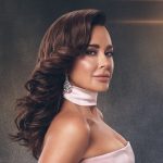 wearing a gown in front of a gray backdrop and spotlight