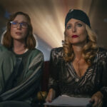 Two women look at what appears to be a movie screen. There's a bright light projected behind them