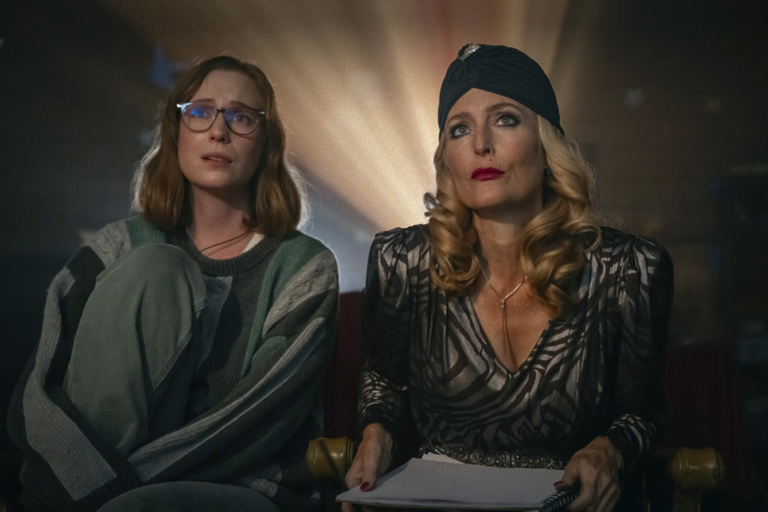 Two women look at what appears to be a movie screen. There's a bright light projected behind them