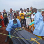 People dressed in protective gear lower into a grave the coffin containing the remains of Jeannine Katusabe, who died of