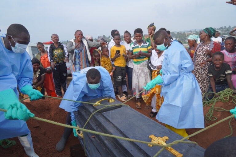 People dressed in protective gear lower into a grave the coffin containing the remains of Jeannine Katusabe, who died of