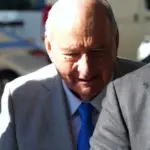 Man in tan suit, white shirt and blue tie in the street