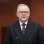 Anthony Albanese, in a dark coat, speaks outside the doors to Parliament