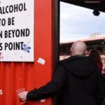 A football fan holds his pint of beer beneath a sign instructing that no alcohol should be taken beyond this point so he can