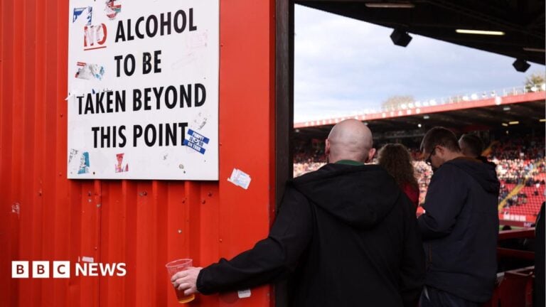 A football fan holds his pint of beer beneath a sign instructing that no alcohol should be taken beyond this point so he can