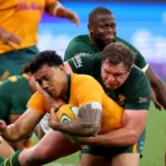 A rugby player in yellow scores a try while being tackled by players in green