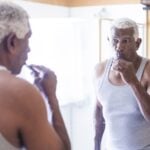 Man brushing his teeth and looking at his reflection in a bathroom mirror