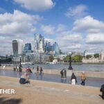 People sit in the autumn sunshine by the London Riverside in London