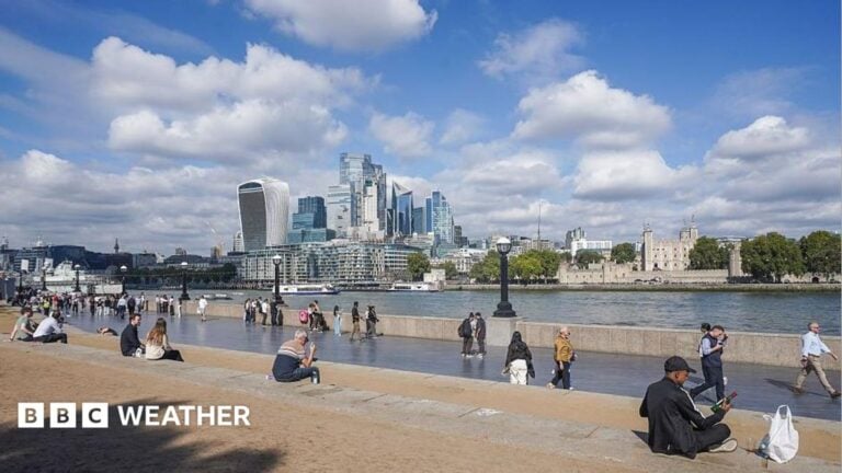 People sit in the autumn sunshine by the London Riverside in London