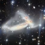 A dark scene with glowing dots on top of it. In the center, there are two wispy galaxies that look tangled in one another
