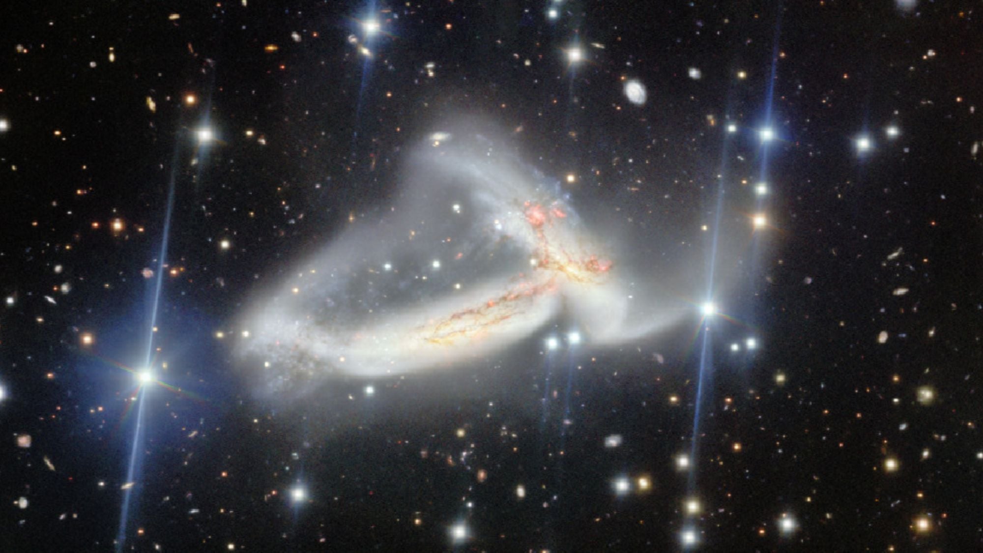 A dark scene with glowing dots on top of it. In the center, there are two wispy galaxies that look tangled in one another