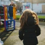 A stock image of a child in a playground. She is facing away form the camera and moving towards a climbing frame. She has a