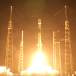 A white rocket blasts off a launch site in the dark early morning