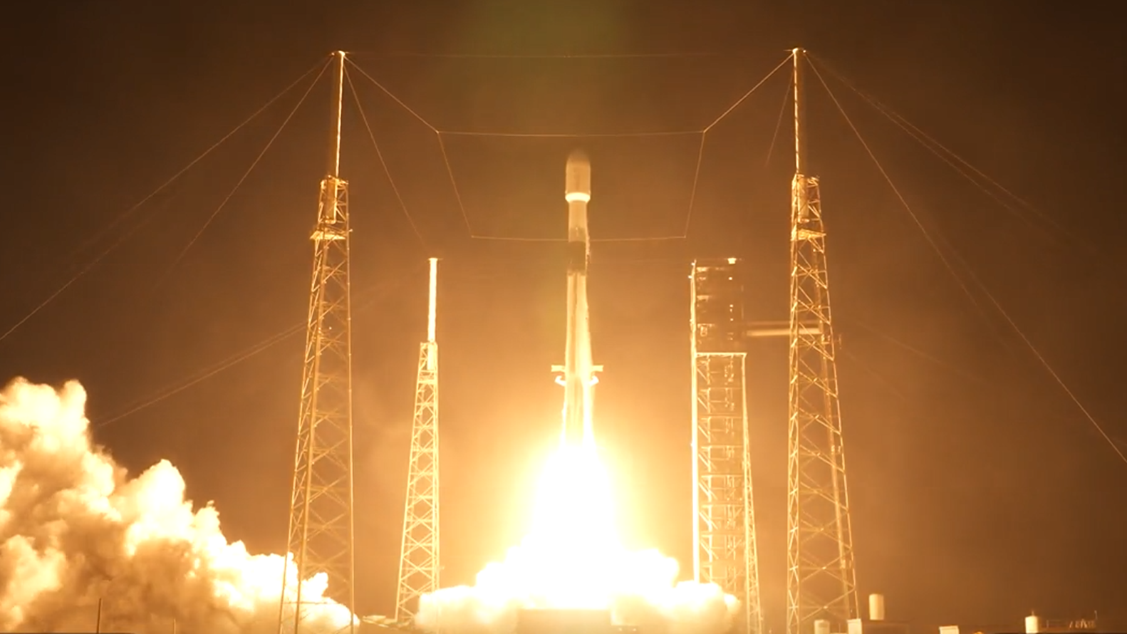 A white rocket blasts off a launch site in the dark early morning