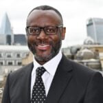 A smiling man in suit and tie standing in front of the City of London skyline