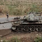 Local farmers walk next to a tank, allegedly of the Eritrean army, that is abandoned along the road in Dansa, southwest of