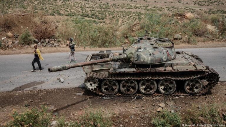 Local farmers walk next to a tank, allegedly of the Eritrean army, that is abandoned along the road in Dansa, southwest of