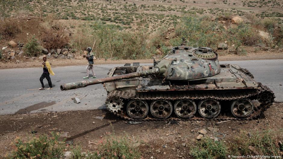Local farmers walk next to a tank, allegedly of the Eritrean army, that is abandoned along the road in Dansa, southwest of