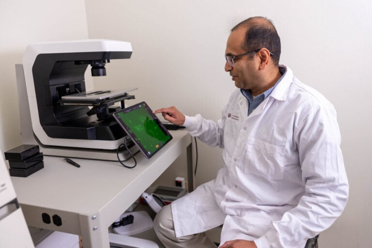 A photo of a researchers in a lab sitting near a machine with a touchscreen monitor