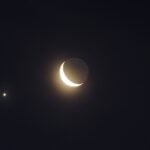 A crescent moon is seen with two small bright stars in the night sky