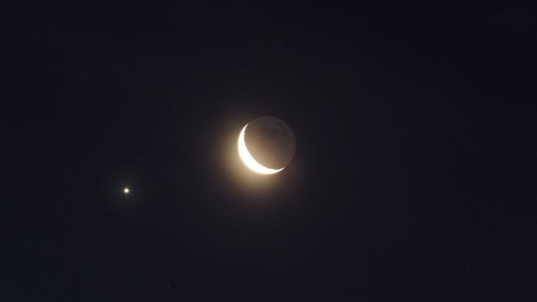 A crescent moon is seen with two small bright stars in the night sky