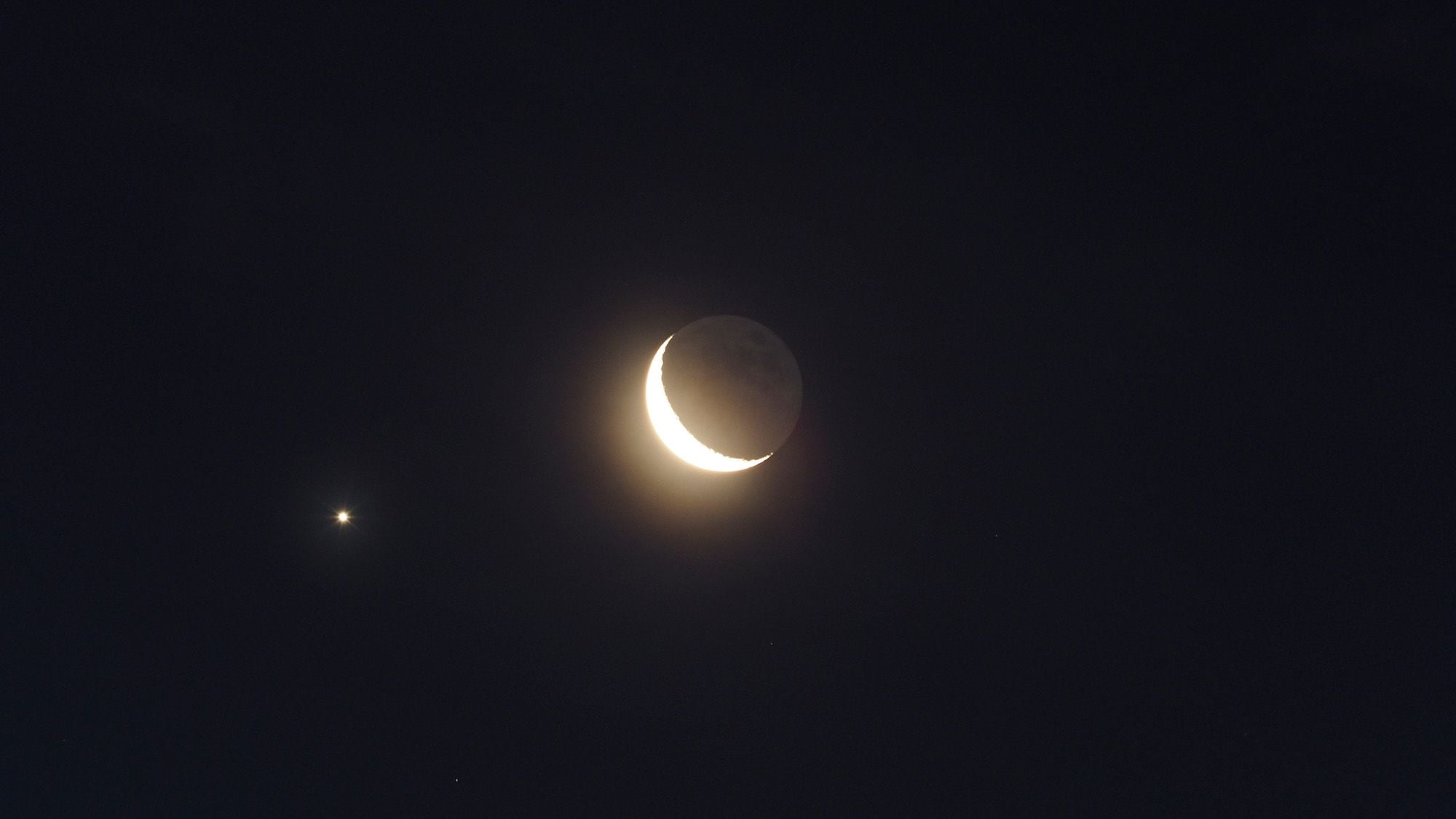 A crescent moon is seen with two small bright stars in the night sky