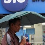 A man walks with an umbrella in front of a Reliance Industries