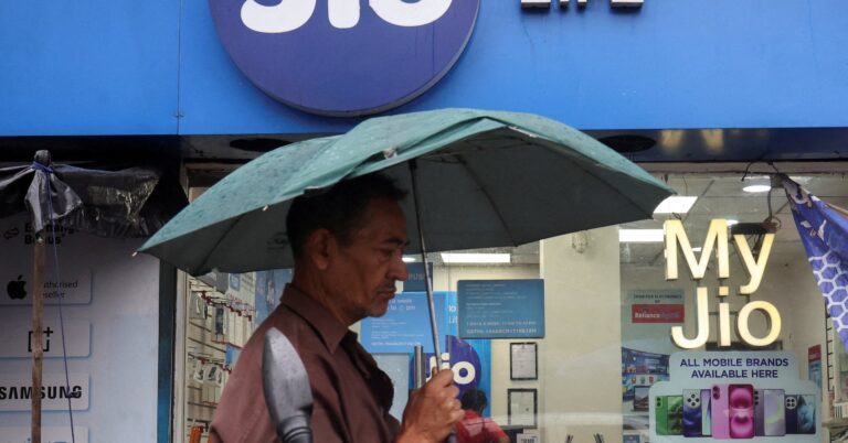 A man walks with an umbrella in front of a Reliance Industries