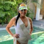 A woman in a white swimming costume with a sash and wearing a visor