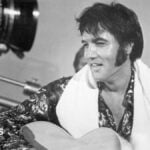 Elvis holding a guitar in a black and white photo from a studio set in 1973