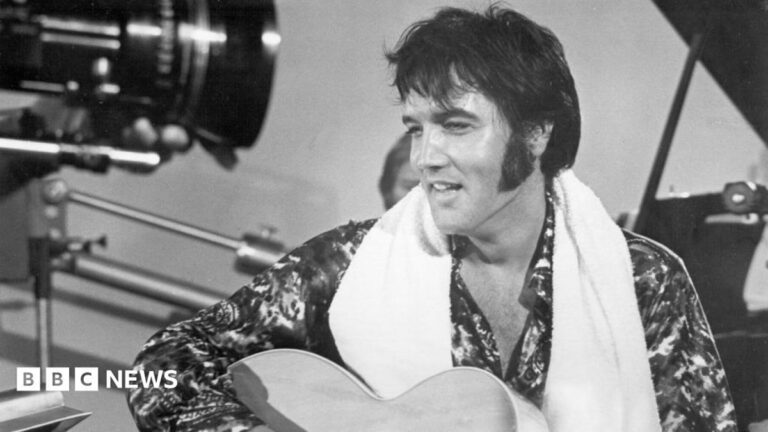 Elvis holding a guitar in a black and white photo from a studio set in 1973