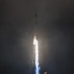 A white rocket blasts off in the dark of night